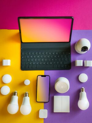 Flat lay of smart home devices including a tablet, smartphone, and bulbs on a vibrant background.