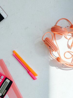Overhead view of a minimalist desktop with headphones, smartphone, and stationery items on a white surface.