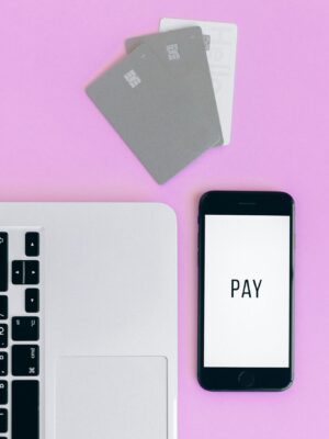 Top view of mobile payment setup with smartphone, credit cards, and laptop on pink background.